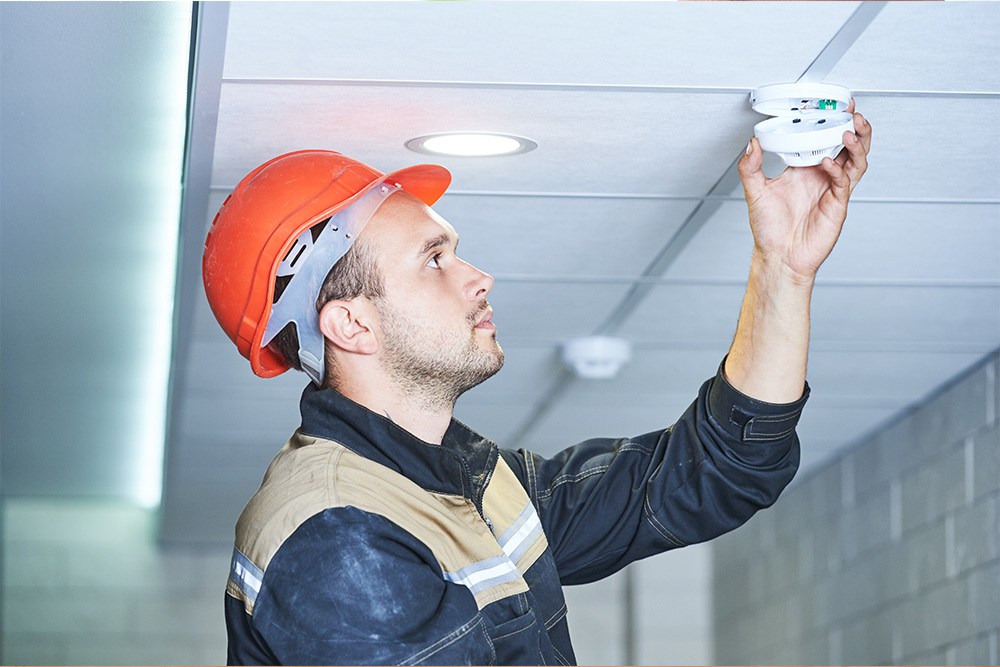 Man in red hard hat testing a fire alarm