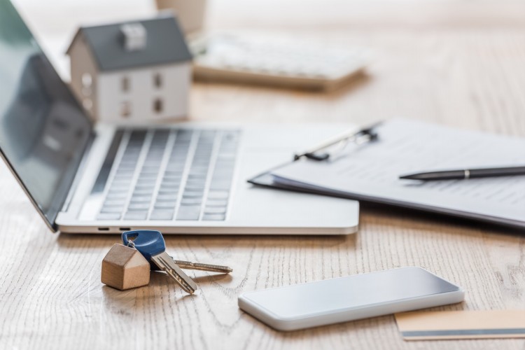 Wooden desk with laptop, clipboard, keys and model house