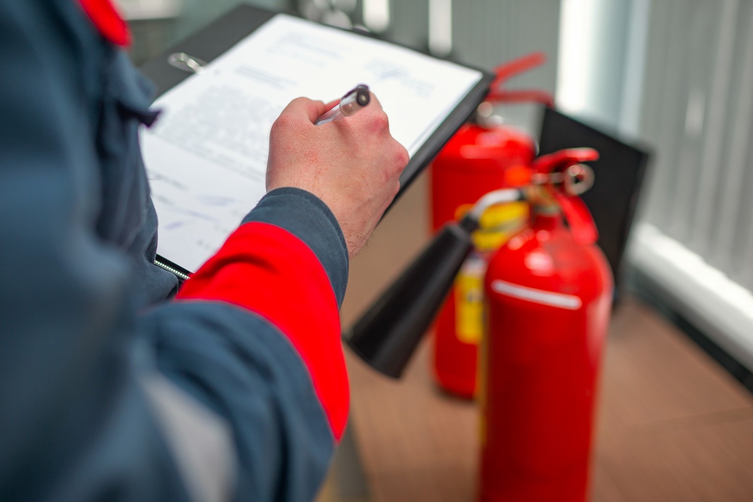 Hand writing on a clip board with blurry fire extinguishers in the background