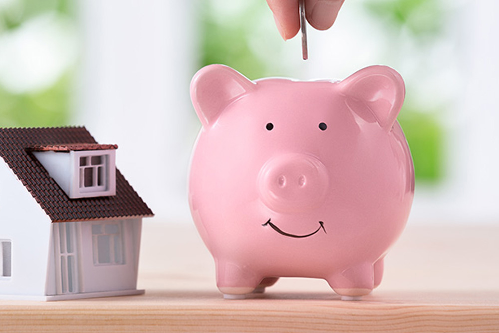 Piggy bank with hand putting coin in, next to a model house