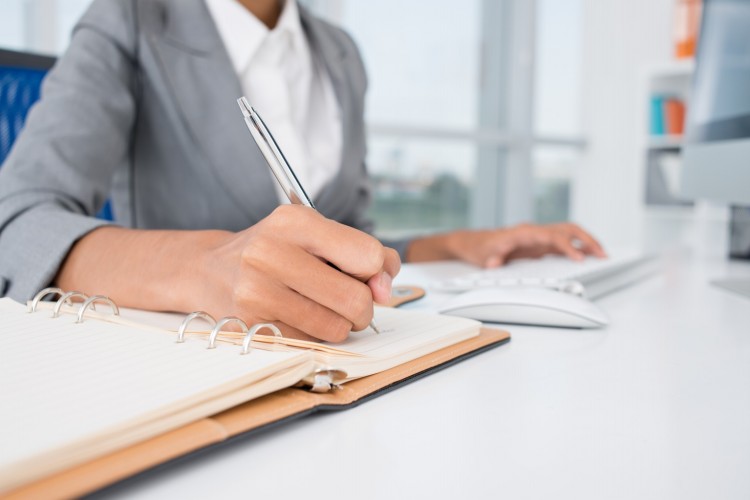 Close up of hands at a computer and writing in a diary