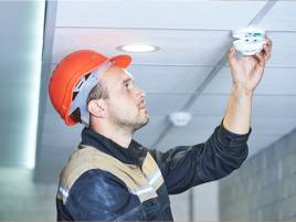 man in hard hat checking a fire alarm